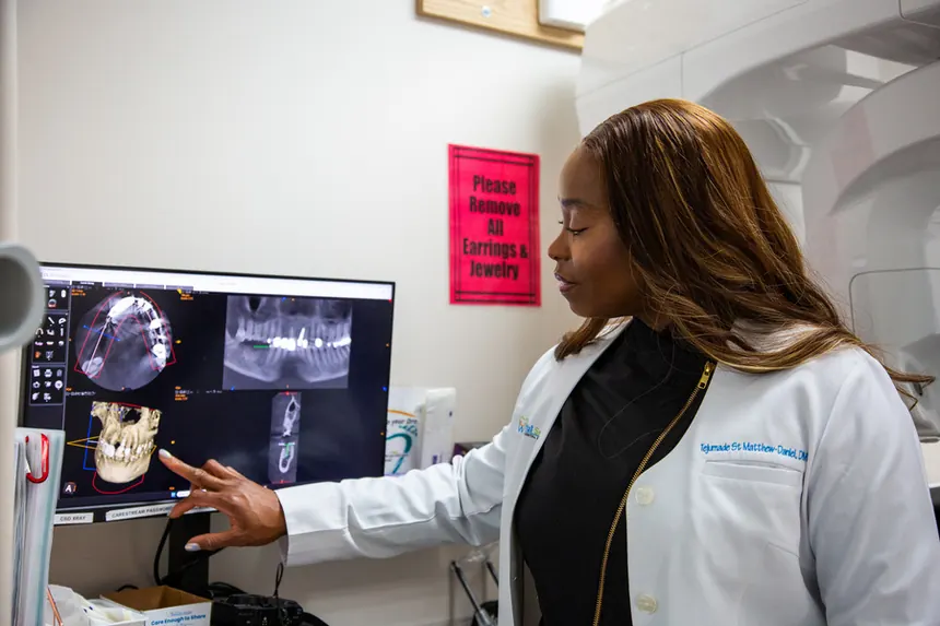 A doctor pointing out details on a dental CT scan display