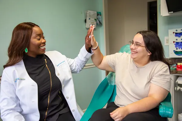 A doctor sharing a high-five with a smiling patient in the dental chair